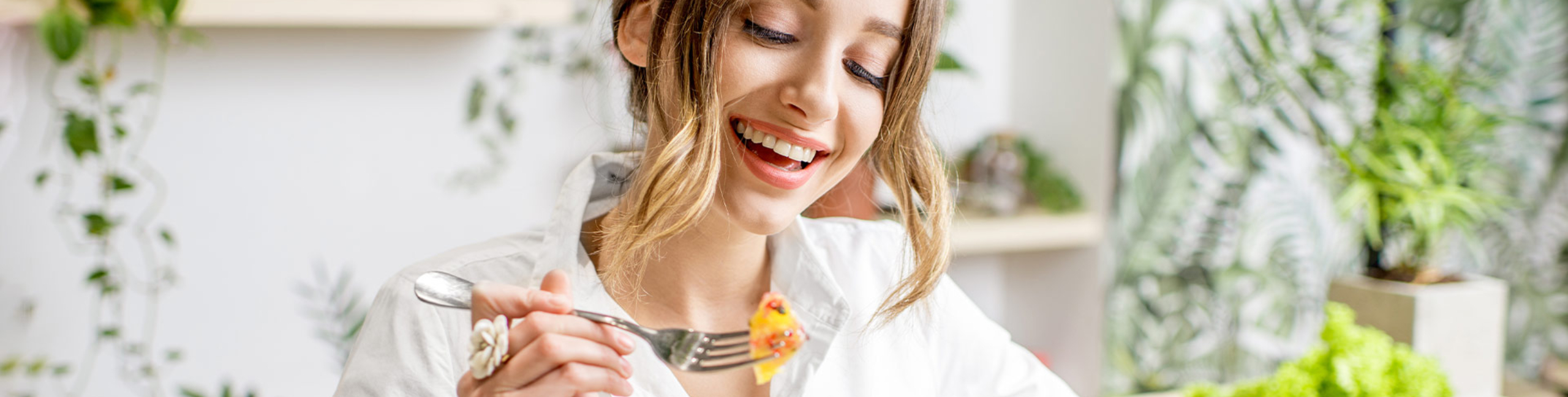 Nasmijana žena jede zdravu salatu za stolom