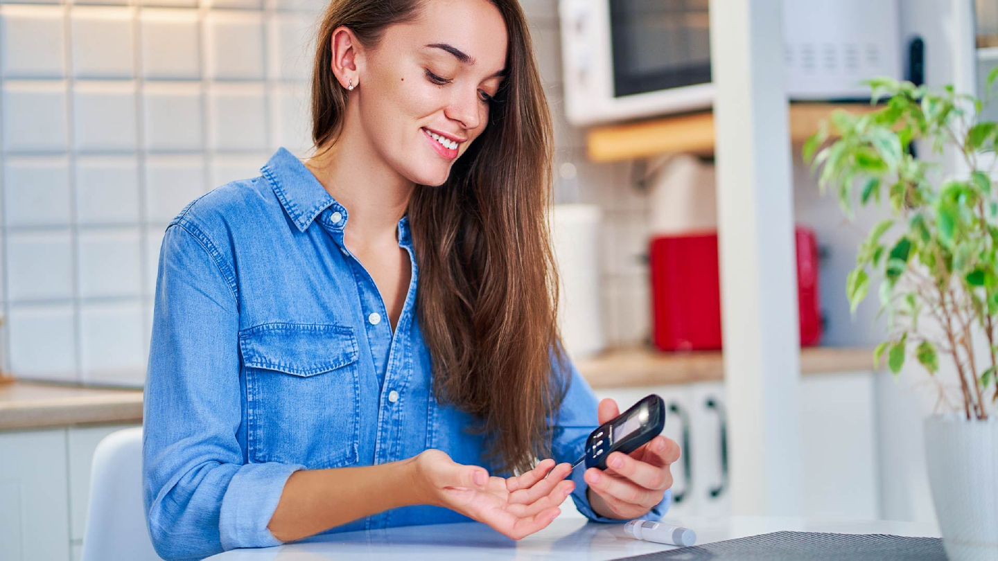 Nasmijana žena mjeri šećer u krvi glukoznim mjeračem