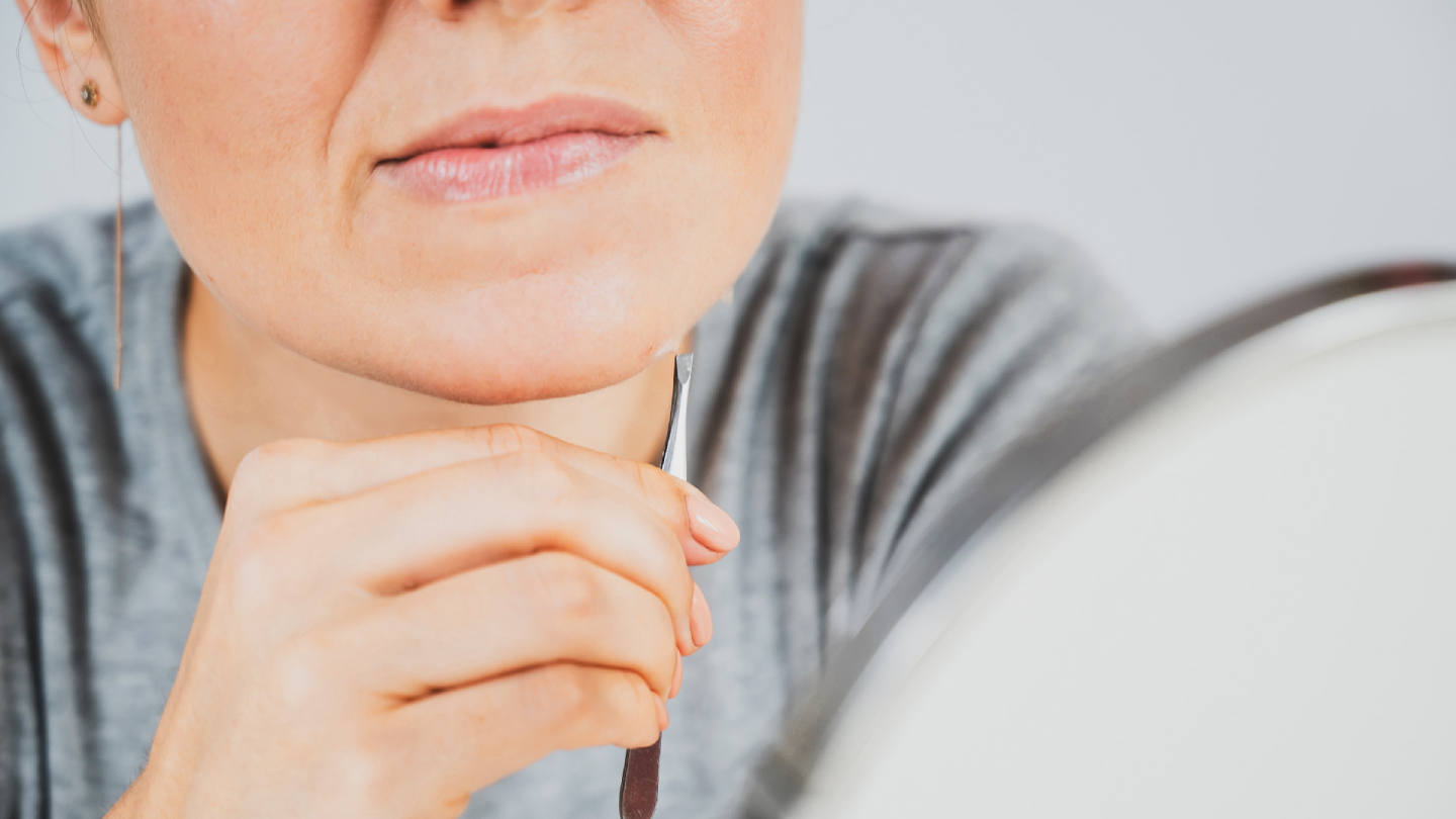 Žena uklanja dlake s brade pincetom, krupni plan